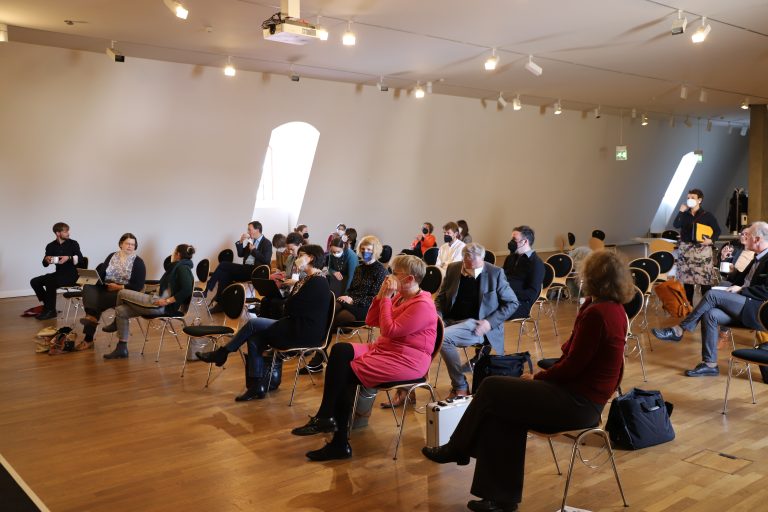 Treffen des Netzwerks Besucher*innenforschung im Jüdischen Museum Berlin am 22. März 2022. Mehrere Personen sitzen in lockeren Stuhlreigen beieinander; sie tragen medizinische Masken.